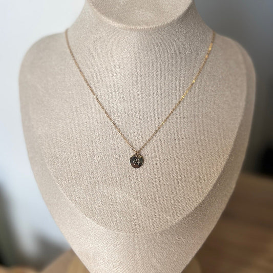 Gold necklace with a pendant on a mannequin bust against a neutral background